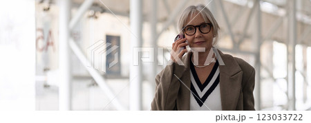 Older woman with glasses talking on the phone while walking in a modern urban setting during the day Older woman with glasses talking on the phone while walking in a modern urban setting during the day 123033722