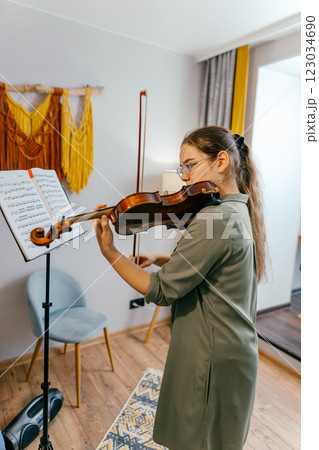 Violin student playing notes at home, preparing for a future performance. A young musician sharpens her violin skills during an intensive rehearsal Violin student playing notes at home, preparing for a future performance. A young musician sharpens her violin skills during an intensive rehearsal 123034690