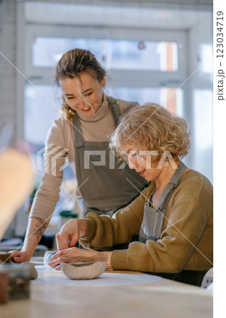 Two women work together with clay, developing skills and enjoying the artistic process. Elderly Caucasian woman learns pottery at a creative workshop with a young mentor 123034719