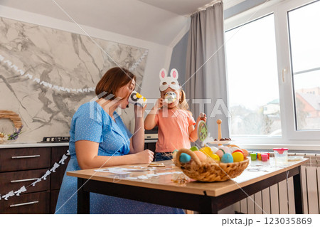 Easter Spring festival. Bottom view of Caucasian happy mother and daughter drink tea and eat festive treats together, sitting in decorated kitchen. Pre-school children's education 123035869