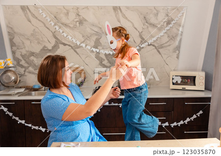 Easter Spring festival. Caucasian Mother plays together with her little happy daughter in rabbit mask, sitting in decorated kitchen 123035870