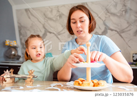 Low angle view of a adult Caucasian mother showing her cute little daughter how to make decorations for the Easter spring holiday. Decoration of the festive table and kitchen 123035876