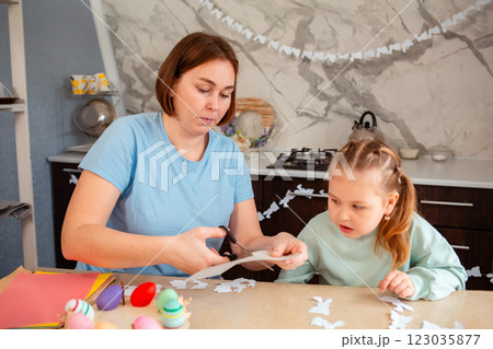 Mid shot of adult young Caucasian mother and her little daughter cut out rabbits out of paper to create decorations for the house. Spring Easter holiday 123035877