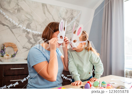 Mother and Caucasian girl and her mother with homemade paper bunny masks are having fun playing in the kitchen. Family Happy Easter Celebration Mother and Caucasian girl and her mother with homemade paper bunny masks are having fun playing in the kitchen. Family Happy Easter Celebration 123035878
