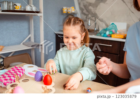 Portrait of Caucasian cute little daughter and her mother are preparing at home for the Easter spring holiday. Festive table and kitchen decoration with handmade decorations 123035879