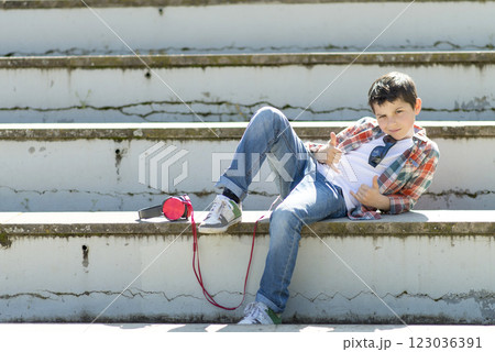 Cool boy reclining on outdoor steps with headphones and shades. 123036391