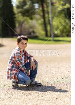 Young boy squatting on a gravel path in a sunny park. Young boy squatting on a gravel path in a sunny park. 123036395