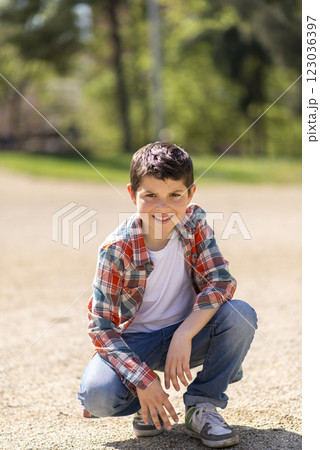 Young boy squatting on a gravel path in a sunny park. Young boy squatting on a gravel path in a sunny park. 123036397