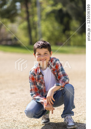 Young boy squatting on a gravel path in a sunny park. Young boy squatting on a gravel path in a sunny park. 123036399