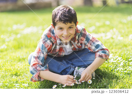 Smiling boy sitting cross-legged on grass in a sunny park. 123036412