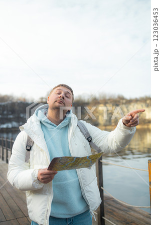 Male hiker wearing backpack reading map during near a lake through forest, discovering scenic wilderness trail with peaceful landscape Male hiker wearing backpack reading map during near a lake through forest, discovering scenic wilderness trail with peaceful landscape 123036453