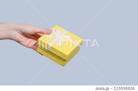 Gift yellow box in hand on blue background. Concept of advertising layout 123036826