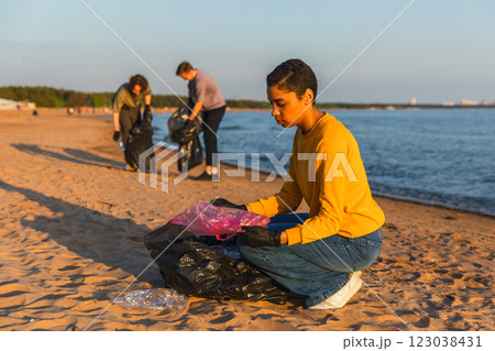 Earth day. Volunteers activists team collects garbage cleaning of beach coastal zone. Woman mans puts plastic trash in garbage bag on ocean shore. Environmental conservation coastal zone cleaning 123038431
