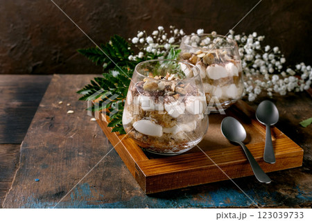 Classic Italian tiramisu layered dessert with cocoa powder and almonds in two glasses. Served on tray with spoons on old wooden table. Decorated white babys breath flowers and green leaves. 123039733