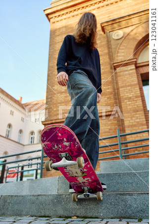 Low angle view of skateboarder balancing on pink skateboard. Close up of underside of deck and wheels of skateboard on stairs at city street 123041161
