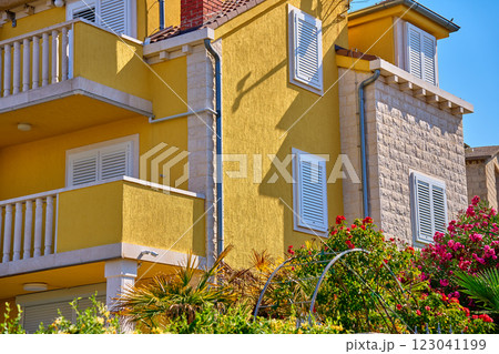 Vibrant yellow villa with white shutters, balcony and lush greenery. Traditional architecture in Croatian village. Rental house for summer vacations in coastal town Vibrant yellow villa with white shutters, balcony and lush greenery. Traditional architecture in Croatian village. Rental house for summer vacations in coastal town 123041199