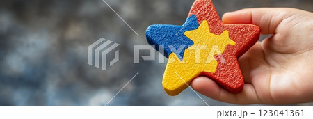 A child's hand holds a colorful star-shaped puzzle, symbolizing the unique pieces that make up autistic individuals. This image is perfect for World Autism Awareness Day 123041361
