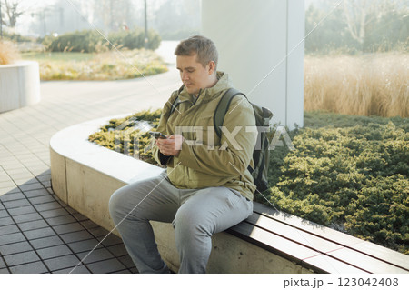 Handsome young man using phone outdoor. Smiling businessman walking outdoors using mobile in urban area. Urban lifestyle concept. Spring time. Handsome young man using phone outdoor. Smiling businessman walking outdoors using mobile in urban area. Urban lifestyle concept. Spring time. 123042408