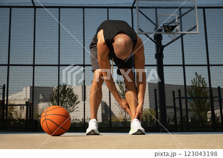 Basketball ankle injury or pain. Basketball player check legs after workout of sport stadium. Professional athlete or sportsman with accident. Man check pain in leg after sport workout. 123043198