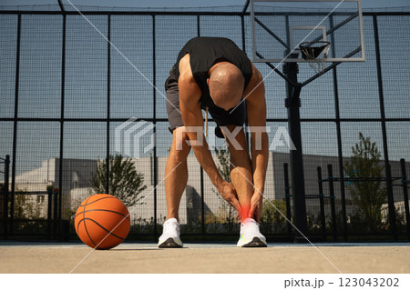 Basketball ankle injury or pain. Basketball player check legs after workout of sport stadium. Professional athlete or sportsman with accident. Man check pain in leg after sport workout. 123043202