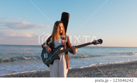Girl Walks And Plays The Bass Instrument On The Beach Near The Ocean At Sunset Girl Walks And Plays The Bass Instrument On The Beach Near The Ocean At Sunset 123046242