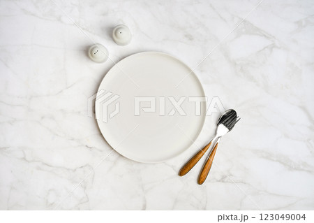 Minimalist dining setup featuring an empty plate and utensils on a marble table Minimalist dining setup featuring an empty plate and utensils on a marble table 123049004