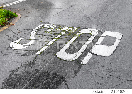 Faded white STOP sign painted on cracked asphalt road with wear and green moss growth. Urban decay. Aging infrastructure. Diagonal angle Faded white STOP sign painted on cracked asphalt road with wear and green moss growth. Urban decay. Aging infrastructure. Diagonal angle 123050202