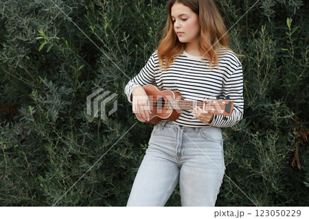 Girl Strums With Ukulele Musical Instrument Near A Tree In The Mountains Girl Strums With Ukulele Musical Instrument Near A Tree In The Mountains 123050229