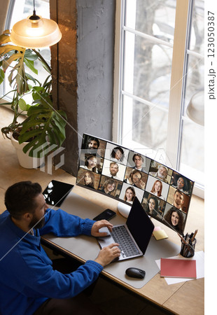 Overhead view of remote professional typing on laptop while participating in large virtual meeting displayed on wide monitor. Overhead view of remote professional typing on laptop while participating in large virtual meeting displayed on wide monitor. 123050387