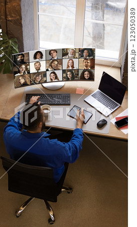 Remote worker in blue sweatshirt using tablet and keyboard while engaged in virtual team meeting displayed on curved screen. 123050389