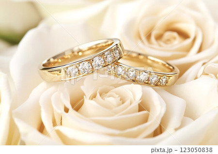 Two golden wedding rings with diamonds resting on white roses 123050838