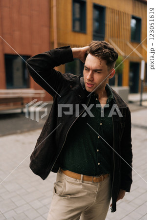 Vertical portrait of stylish man adjusting hair while walking down street, radiating confidence and urban charm in trendy attire, showcasing modern and fashionable lifestyle amidst city architecture 123051619