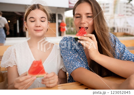 Two women enjoy watermelon slices at an outdoor market during summer, showcasing a joyful summer scene. 123052045