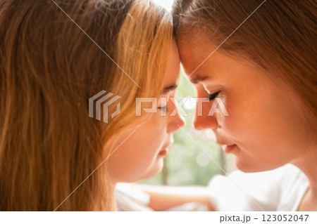 Sisters Foreheads Touching Indoor Closeup: Affectionate bond between two young sisters touching foreheads indoors, showcasing intimacy and love. 123052047