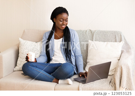 Working From Home Concept. Black Millennial Girl Using Laptop At Home For Freelance Work, Sitting On Sofa And Drinking Coffee, Copy Space Working From Home Concept. Black Millennial Girl Using Laptop At Home For Freelance Work, Sitting On Sofa And Drinking Coffee, Copy Space 123053125