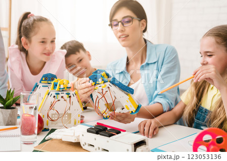 A group of young students are learning about robotics and engineering in a classroom setting. A teacher is helping them build and program a robot, while they work together and ask questions. A group of young students are learning about robotics and engineering in a classroom setting. A teacher is helping them build and program a robot, while they work together and ask questions. 123053136