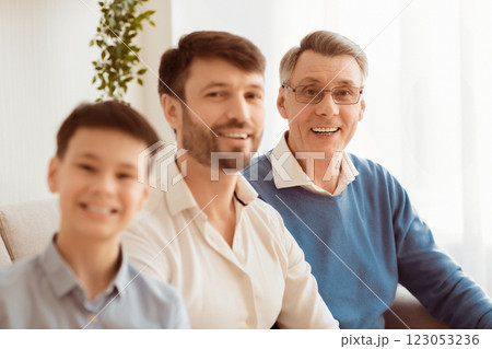 Multi-Generational Family. Joyful Senior Man, His Adult Son And Grandson Boy Smiling At Camera Sitting On Sofa At Home. Multi-Generational Family. Joyful Senior Man, His Adult Son And Grandson Boy Smiling At Camera Sitting On Sofa At Home. 123053236