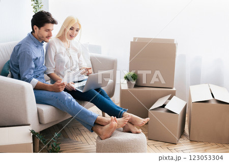 Buying House. Cheerful Couple Using Laptop Looking Through Ownership Papers Sitting On Sofa After Moving Apartment. Free Space Buying House. Cheerful Couple Using Laptop Looking Through Ownership Papers Sitting On Sofa After Moving Apartment. Free Space 123053304