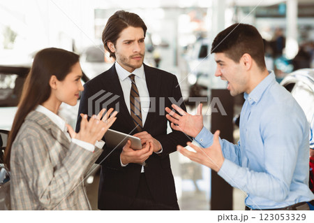 Car Seller Looking At Couple Having Quarrel About Buying Too Expensive Car In Dealership Showroom. Selective Focus Car Seller Looking At Couple Having Quarrel About Buying Too Expensive Car In Dealership Showroom. Selective Focus 123053329