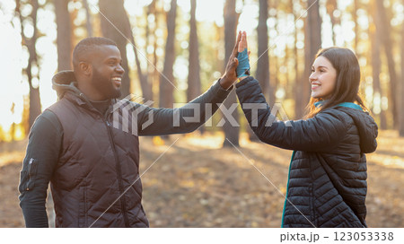 African guy giving girl high five to pretty girl over tent, camping in autumn forest, copy space 123053338