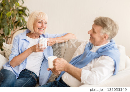 Happy senior couple with coffee cups sitting on sofa and talking, enjoying time together 123053349