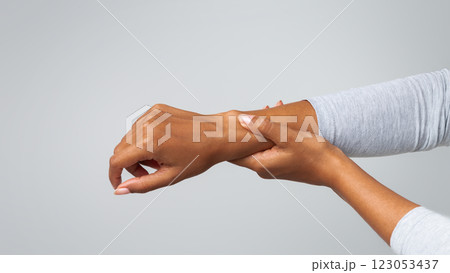 Young afro woman suffering from arthritis, rubbing her wrist, cropped, grey background 123053437