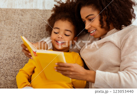 Cute Black Mother And Little Daughter Reading Book Together Sitting On Couch At Home. Bedtime Story Concept 123053440