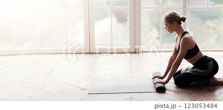 Side view of young yoga girl after meditation, rolling yoga mat over big panoramic window, copy space 123053484