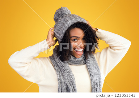 Happy Winter Holidays. Smiling black woman wearing gray knitted hat and scarf over yellow studio background 123053543