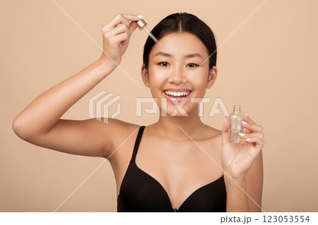 Skincare. Beautiful Asian Girl Applying Cosmetic Oil On Face Skin Standing Over Gray Background. Studio Shot 123053554
