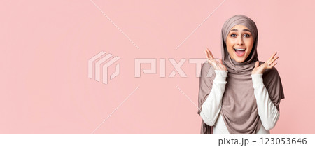 Wow. Surprised muslim girl in headscarf opened mouth in amazement over pink studio background, panorama with free space 123053646