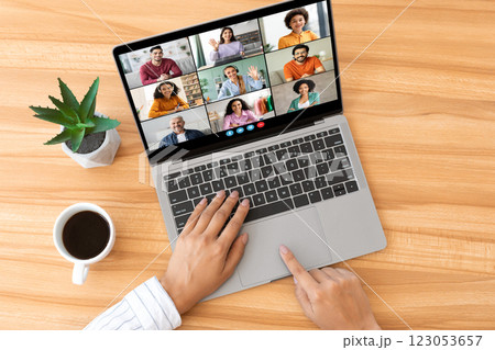 A person is sitting at a wooden desk, using a laptop to participate in a video conference. There are multiple participants visible on the screen, top view 123053657