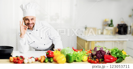 Cooking Food. Positive Chef Man Gesturing Okay Standing Next To Work Table In Kitchen Indoor. Selective Focus Cooking Food. Positive Chef Man Gesturing Okay Standing Next To Work Table In Kitchen Indoor. Selective Focus 123053711