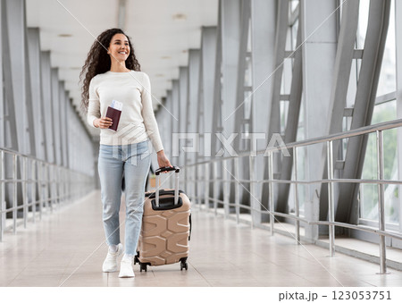Happy Young Smiling Woman Walking With Luggage At Airport Terminal, Cheerful Middle Eastern Female Holding Passport With Tickets And Carrying Suitcase While Going To Flight Departure Gate, Copy Space 123053751